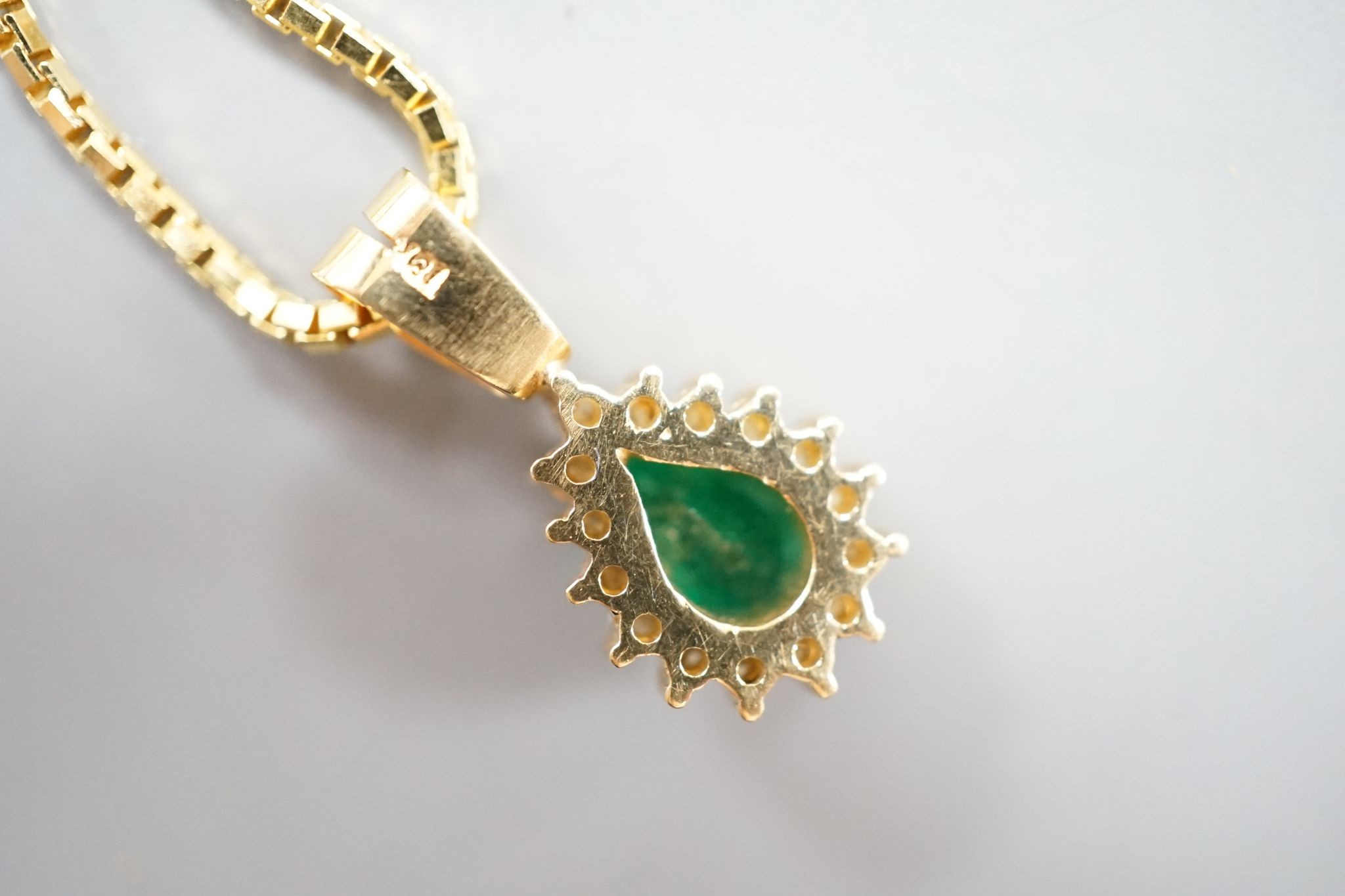 A modern 18k, emerald and diamond cluster set pear shaped pendant, overall 21mm, on an 18k chain, 43cm
